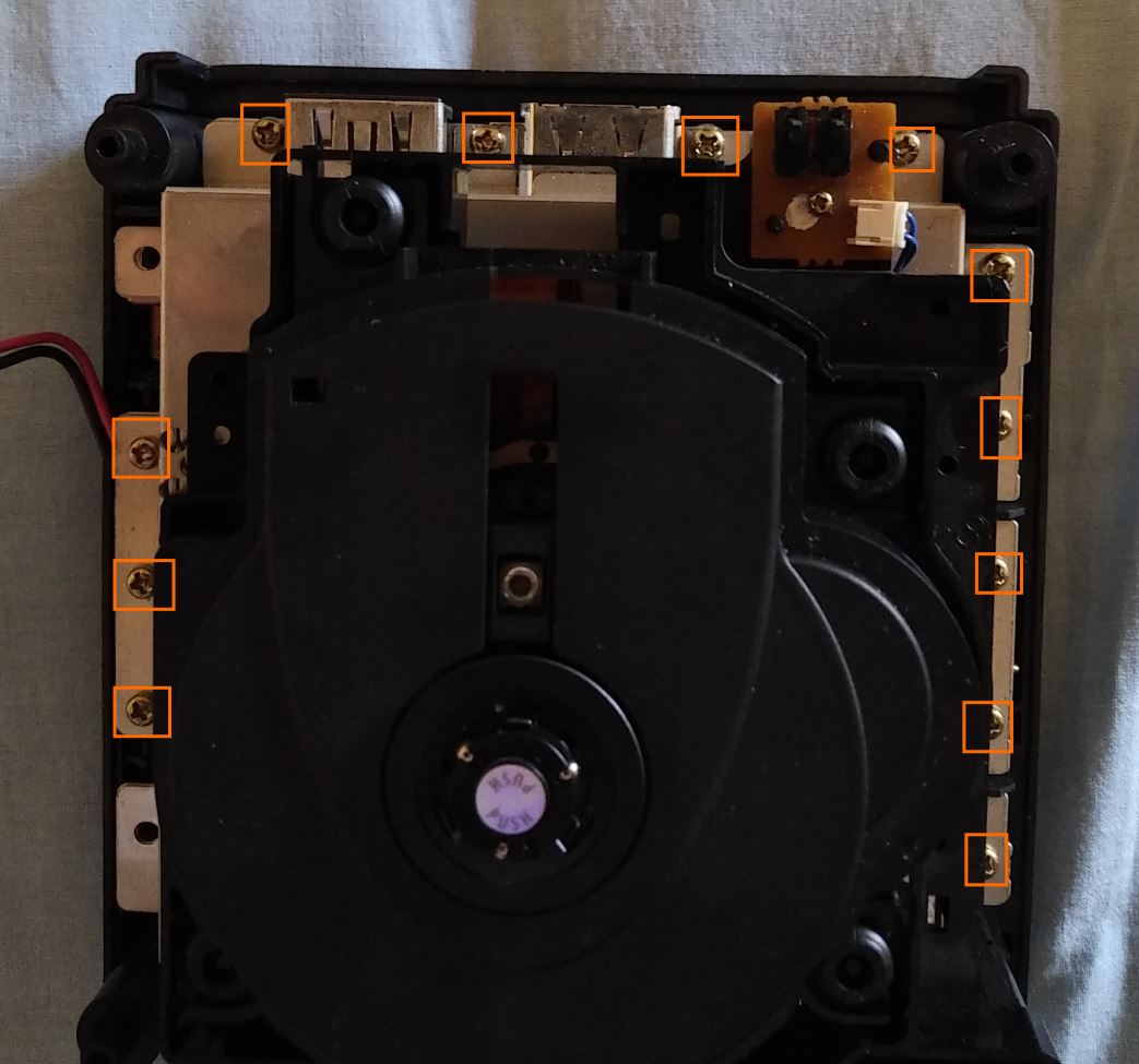 Top view of console, with 3 out of 5 screws on the left under the fan, 4 on the back between the video porta, and 5 to the right - all to be removed